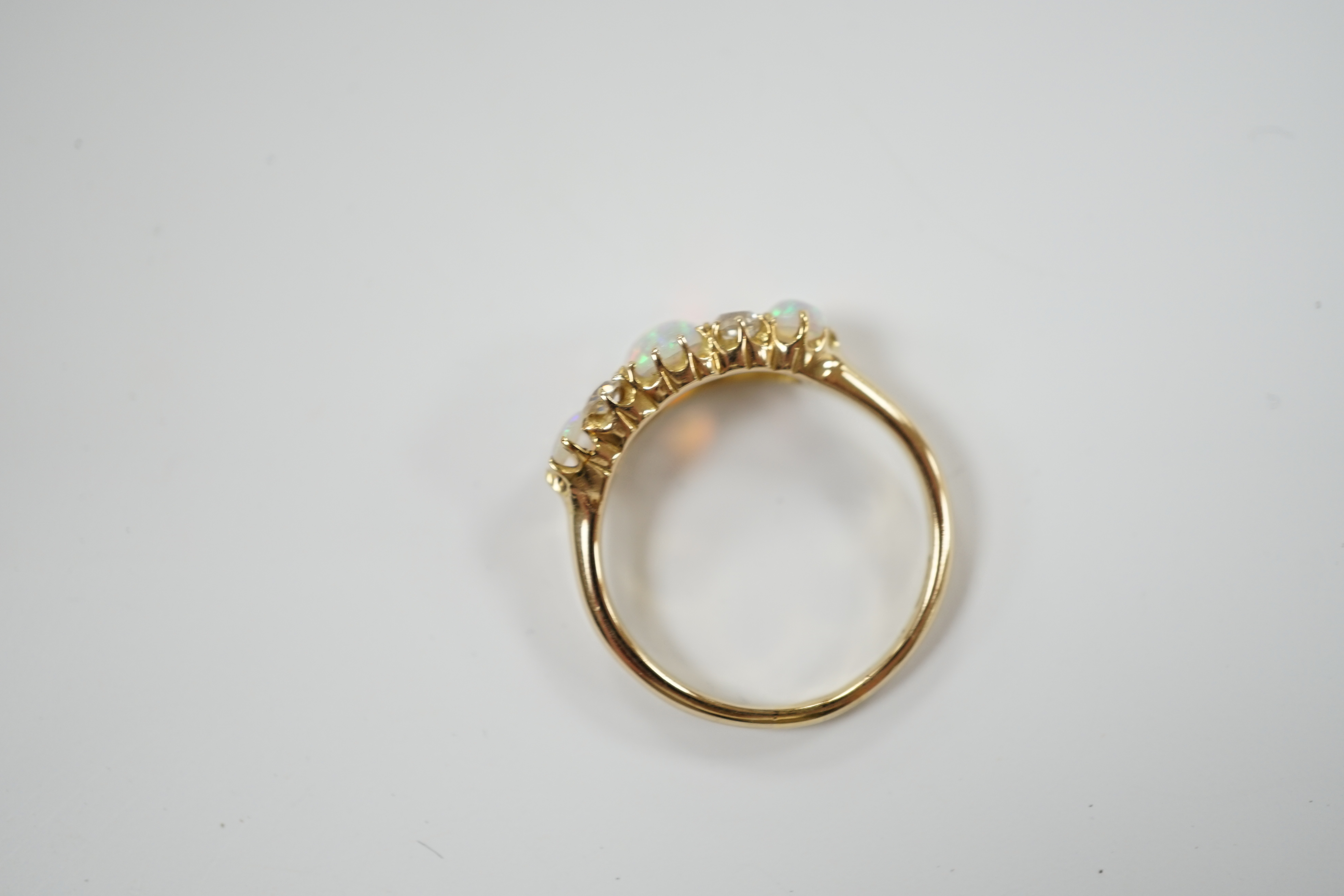 A yellow metal (tests as 18ct), three stone white opal and four stone diamond set half hoop ring, size N/O, gross weight 3.5 grams.